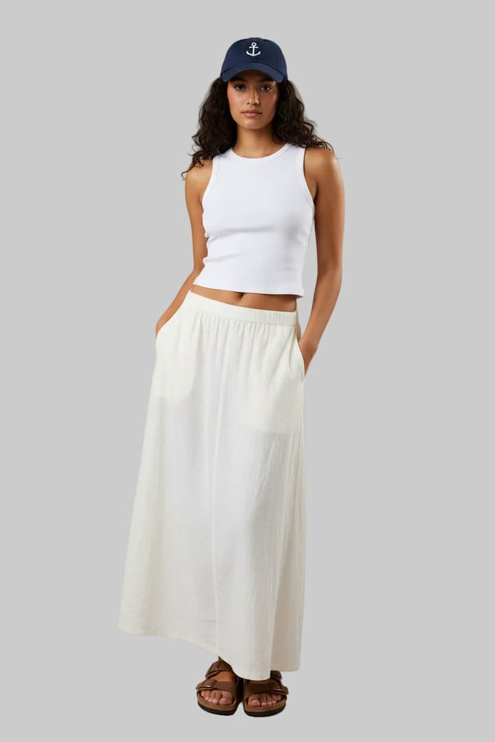 Woman wearing a white tank top and blue jeans with a blue cap on a beige background