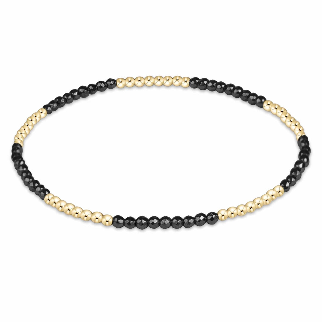 A beaded enewton  stretch bracelet featuring alternating sections of polished gold and matte black round beads, arranged in an oval shape on a plain white background.