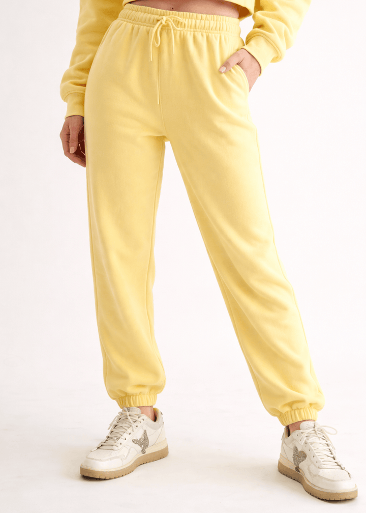 Person wearing a yellow tracksuit with white sneakers on a light gray background